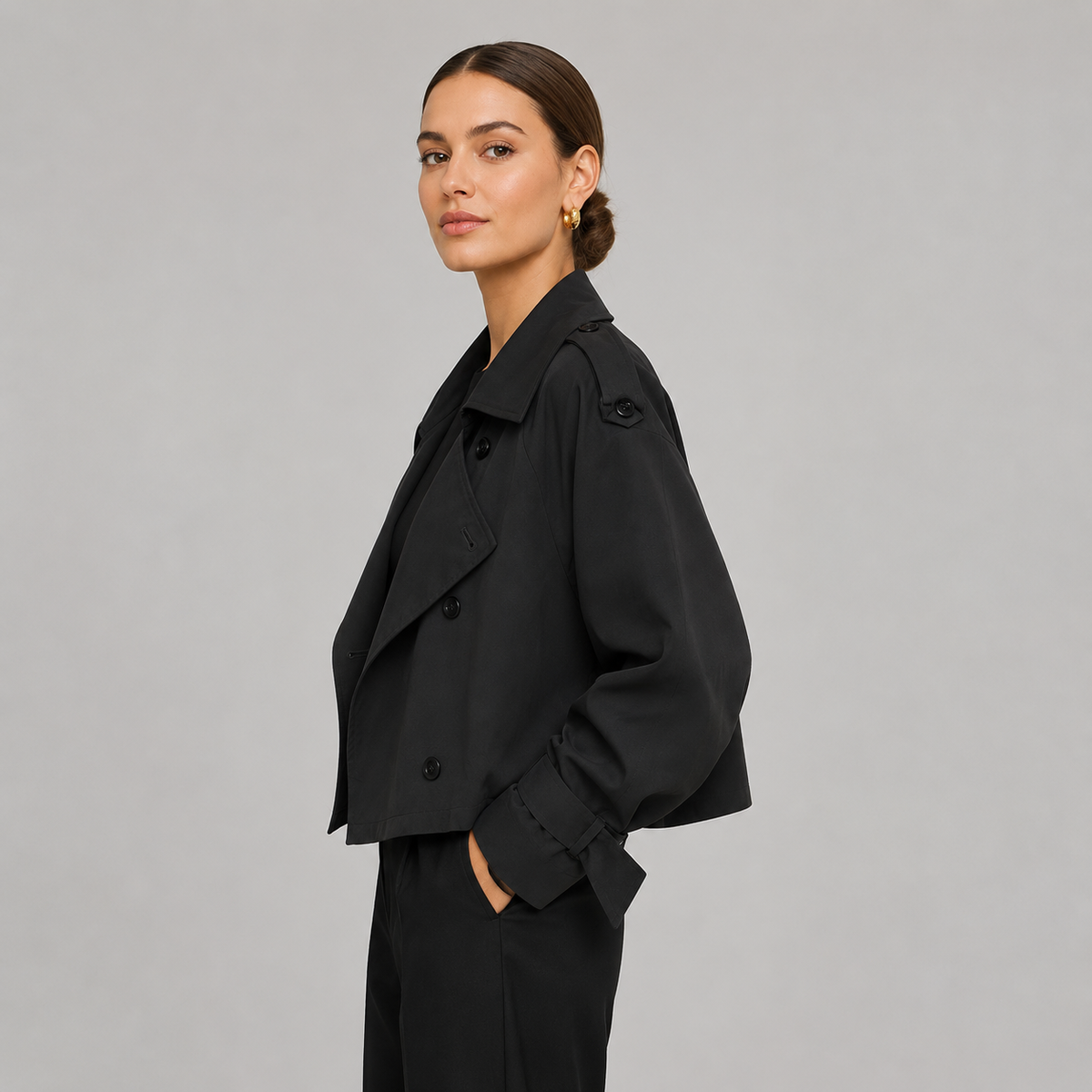 Modelo con gabardina corta cruzada en negro, vista de perfil