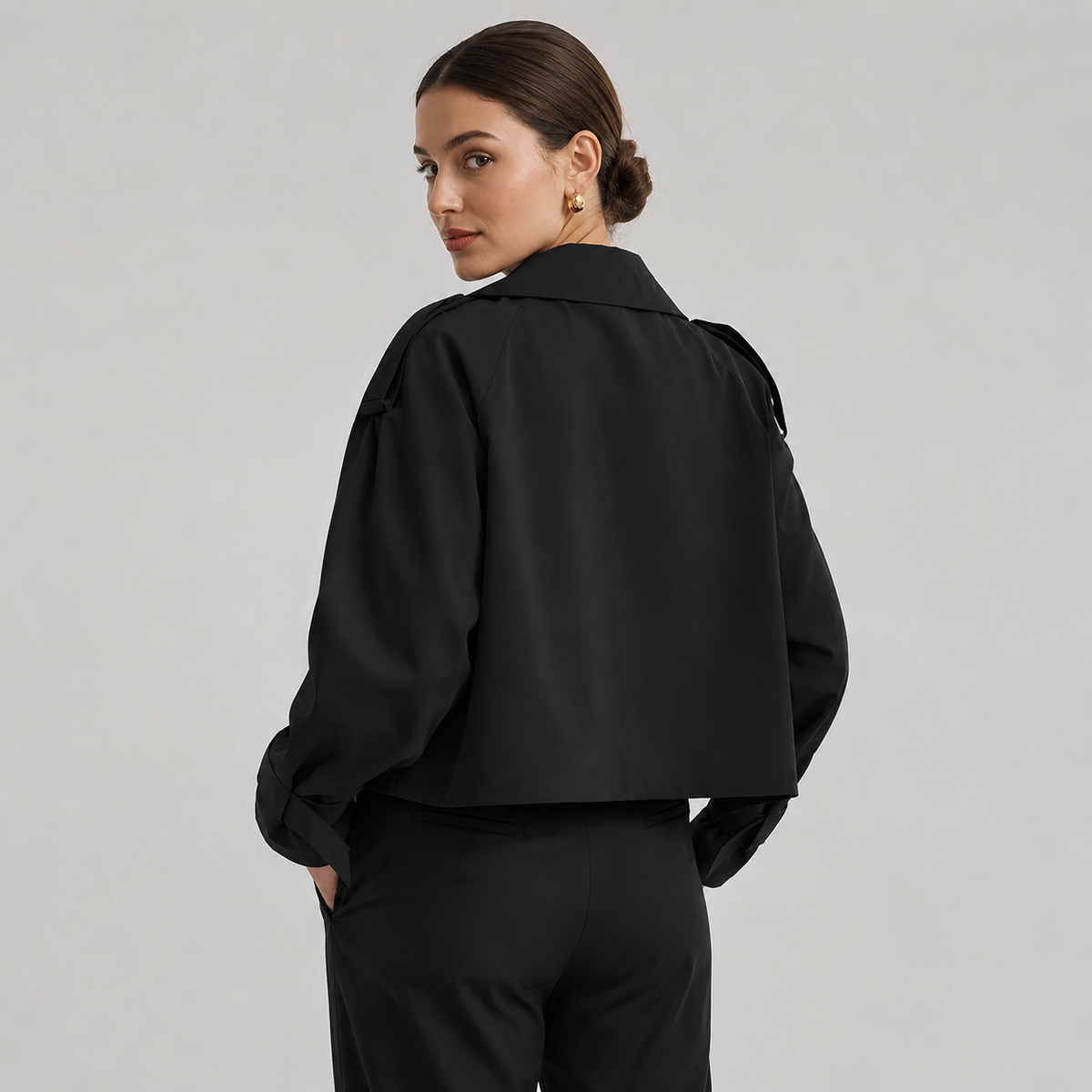 Modelo con gabardina corta cruzada en negro, vista trasera